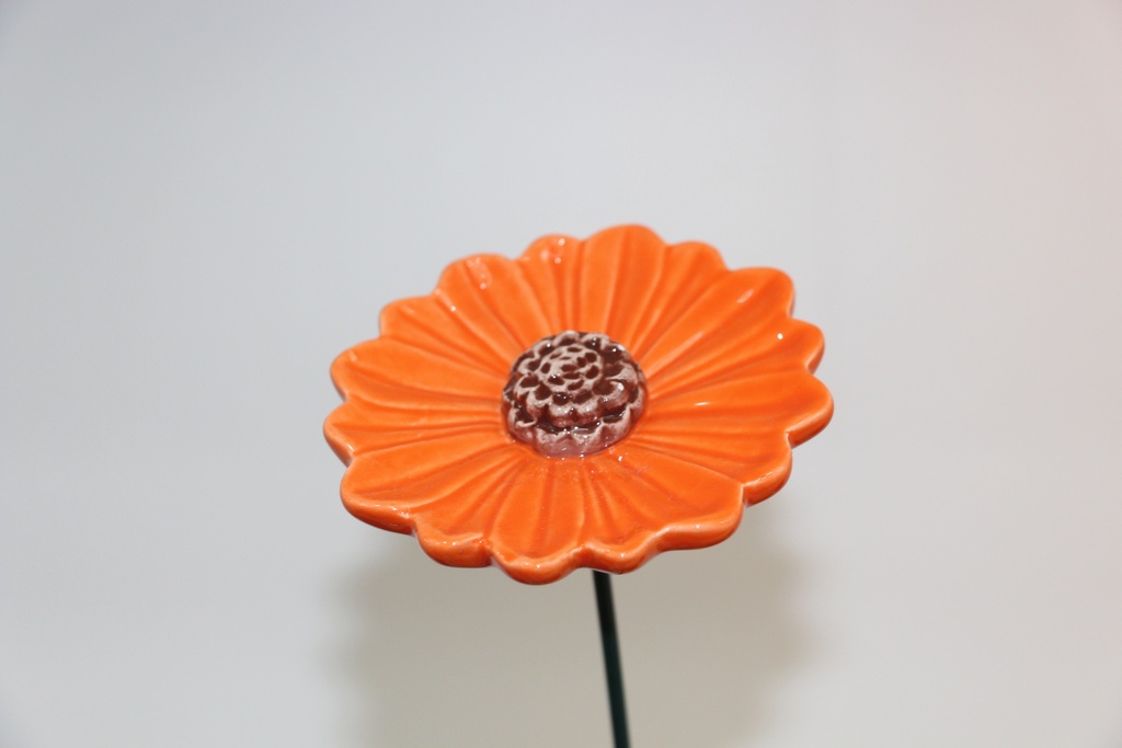 Flor decorativa em cerâmica laranja com centro em espiral e haste metálica