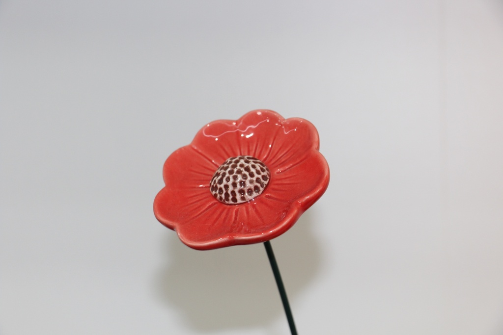 Flor decorativa em cerâmica vermelha com centro pontilhado e haste metálica