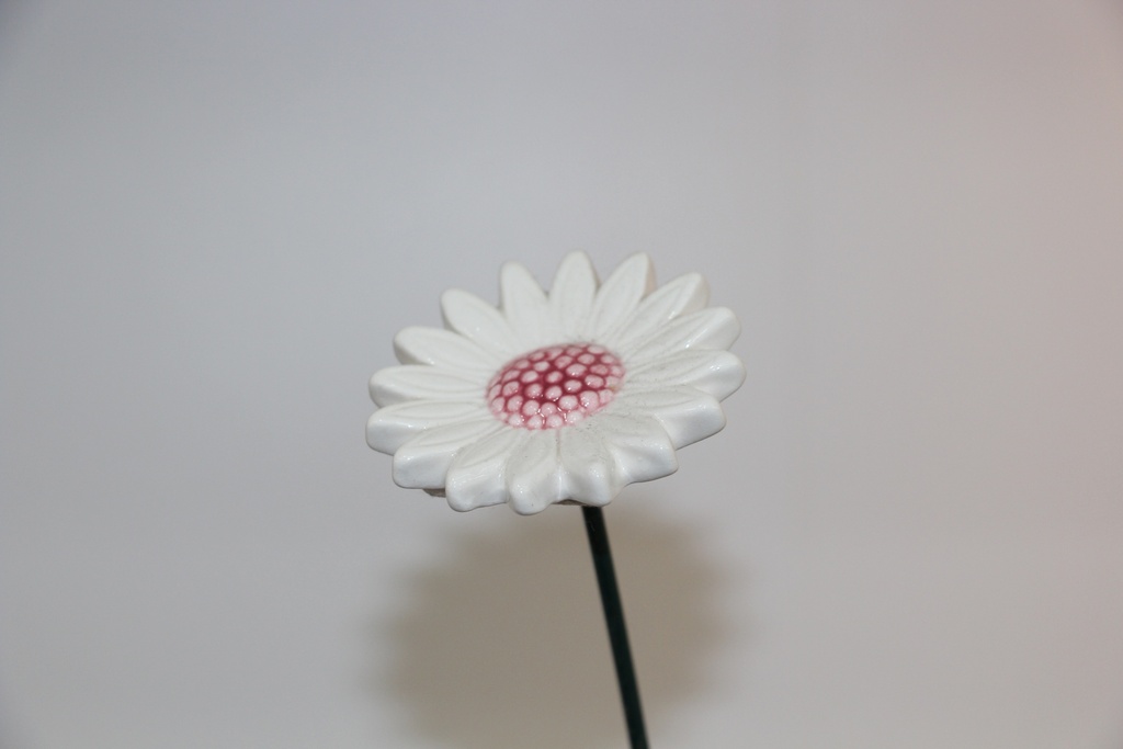 Flor decorativa em cerâmica branca com centro rosado e haste metálica