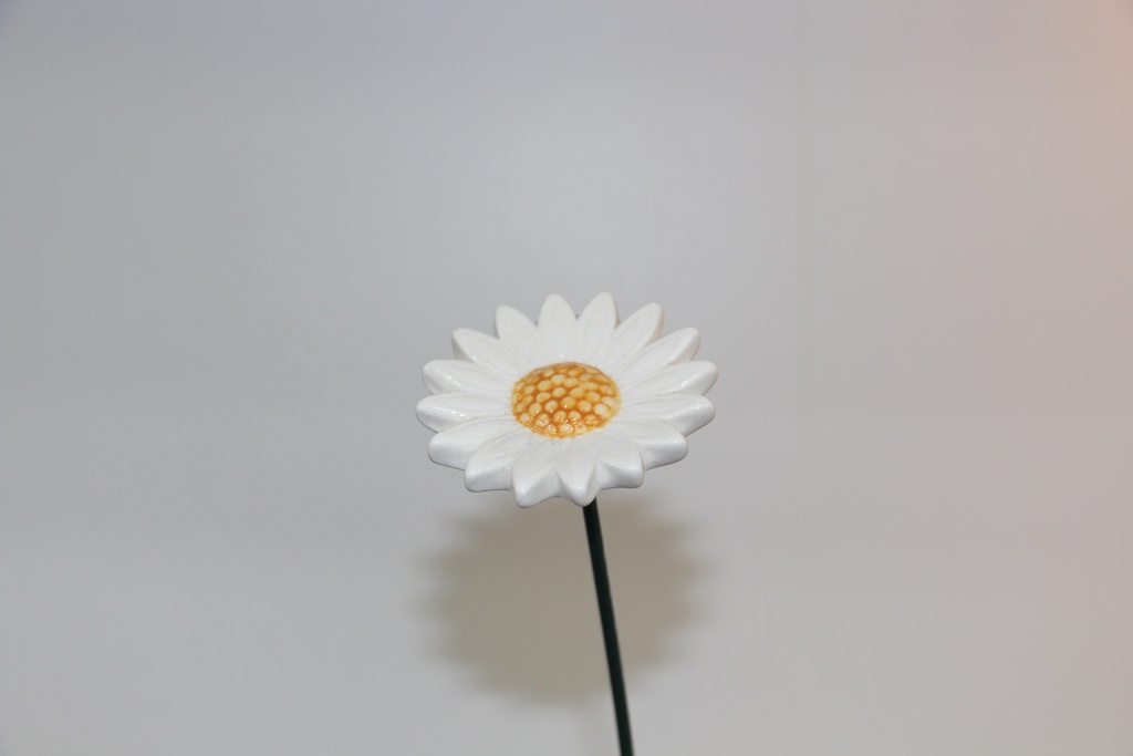 Flor decorativa em cerâmica branca com centro amarelo e haste metálica