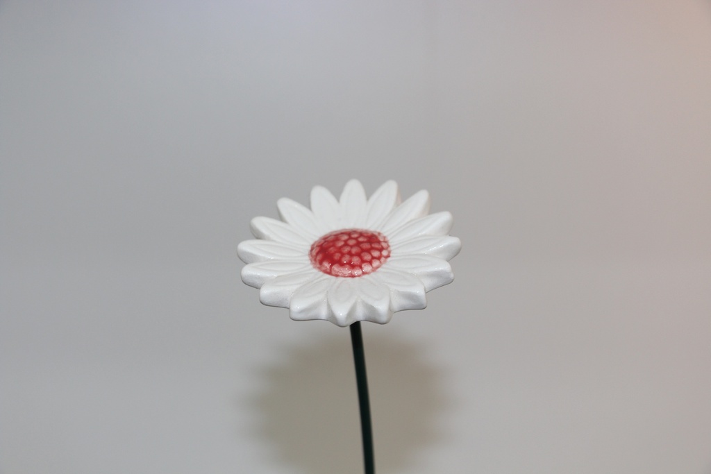 Flor decorativa em cerâmica branca com centro vermelho e haste metálica