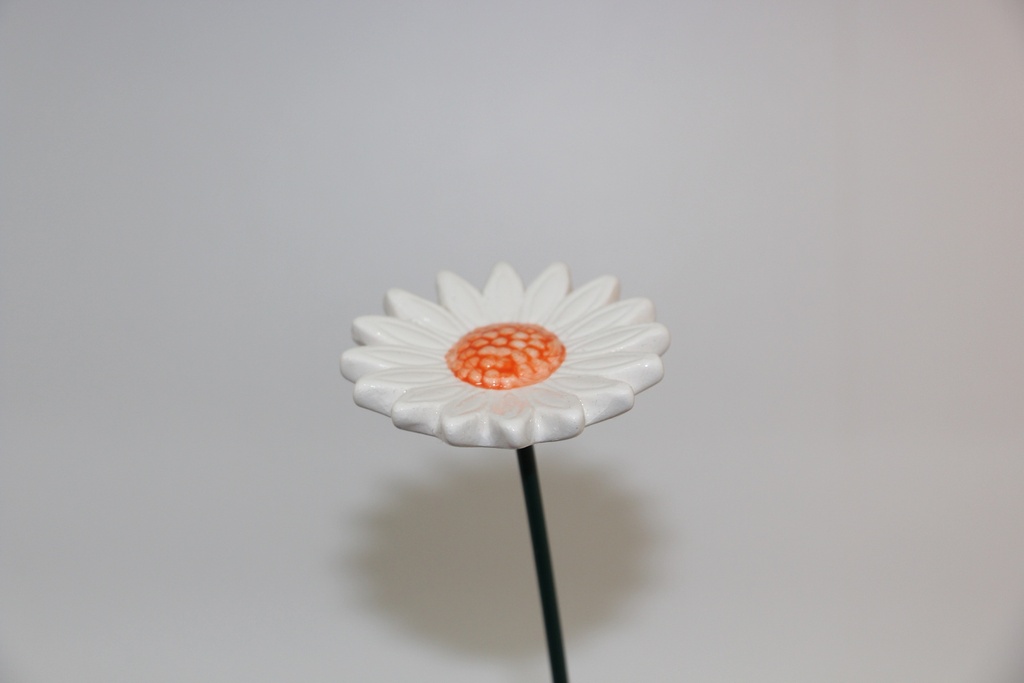 Flor decorativa em cerâmica branca com centro laranja e haste metálica