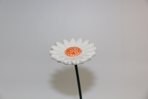 Flor decorativa em cerâmica branca com centro laranja e haste metálica